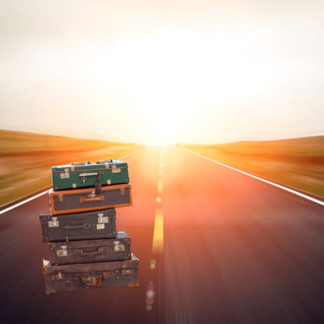 An open road leading into sunset. At the front site a wobble stack of baggage