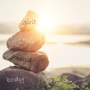 Sunset background. In front is a stack of rocks with the words body, mind, soul, spirit.